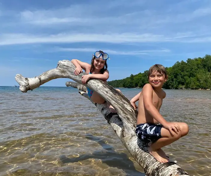 Two children sitting on a tree branch in the water.