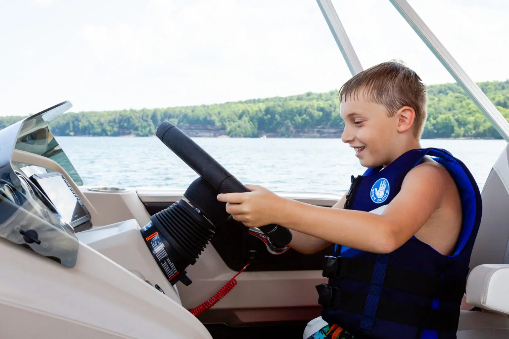 A boy in life vest driving boat on water.