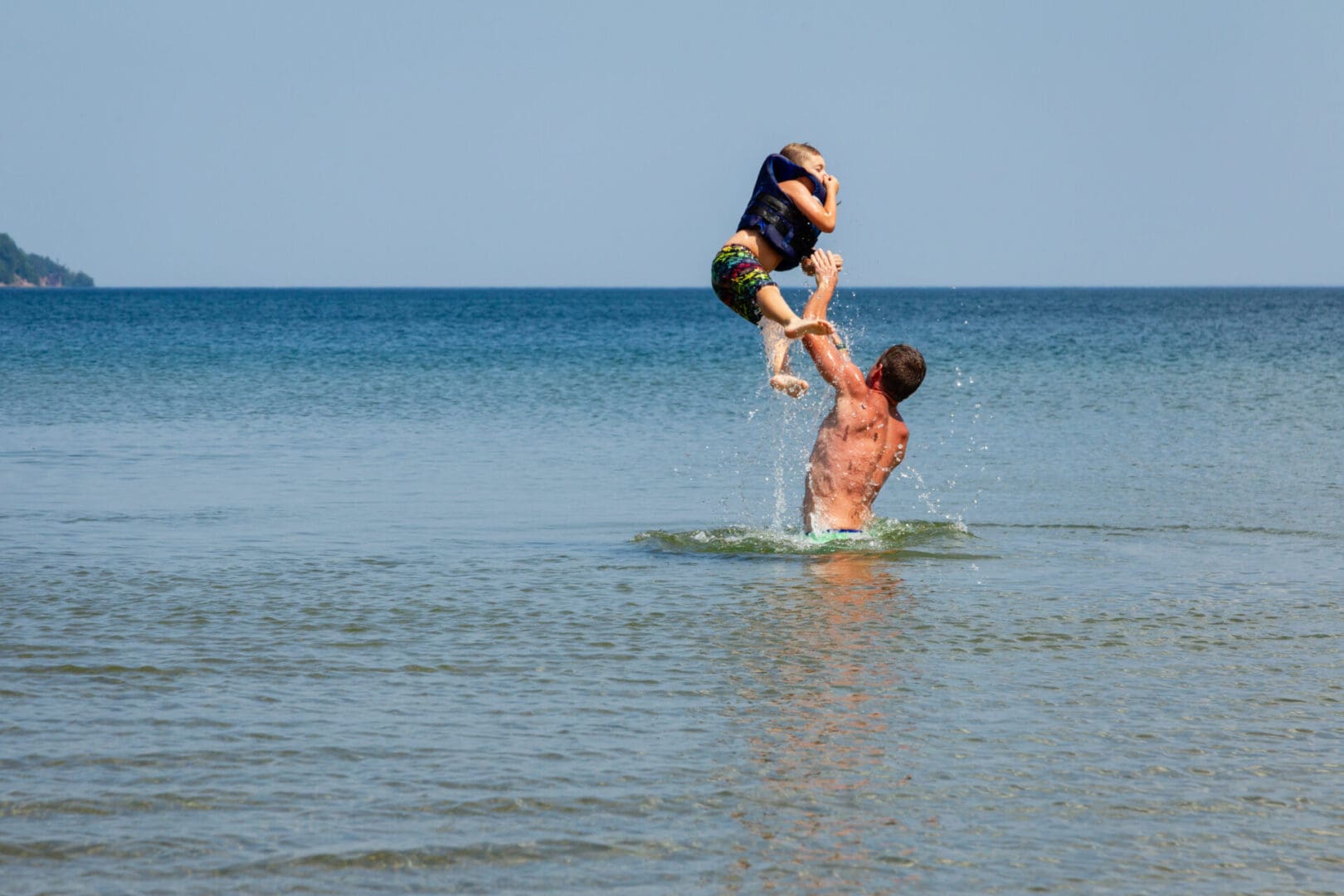 A man is jumping in the water while another person jumps over him.