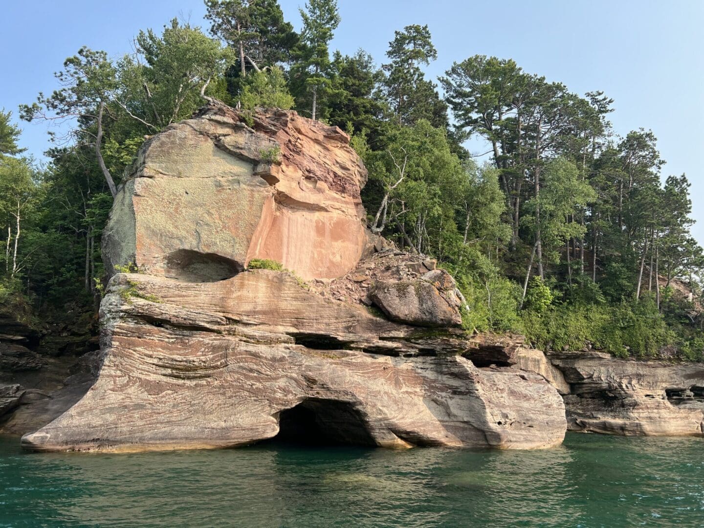 A rock formation in the water near trees.