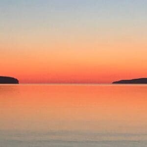 A sunset over the ocean with two islands in the distance.