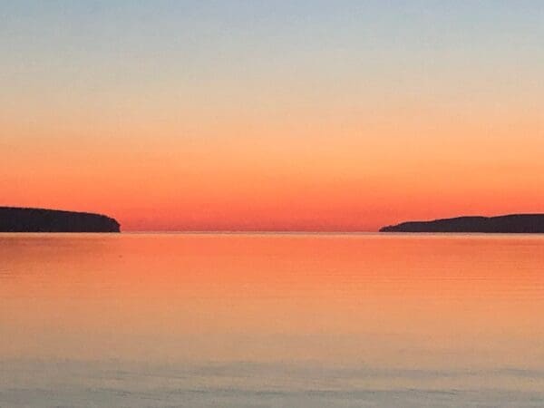 A sunset over the ocean with two islands in the distance.